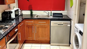 A compact kitchen with wooden cabinets, a microwave, a sink, a dishwasher, and a washing machine. - 4 bedroom duplex in central London with private entrance (London)