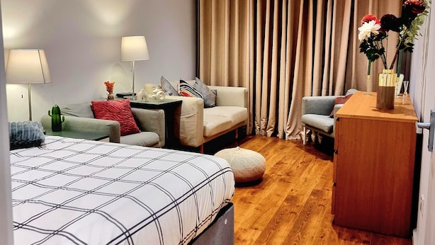 A hotel room with a bed, a desk, a chair, a small table with a vase, and a window with curtains. - 4 bedroom duplex in central London with private entrance (London)
