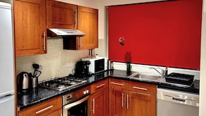 A kitchen with wooden cabinets, a gas stove, a microwave, a dishwasher, and a red accent wall. - 4 bedroom duplex in central London with private entrance (London)