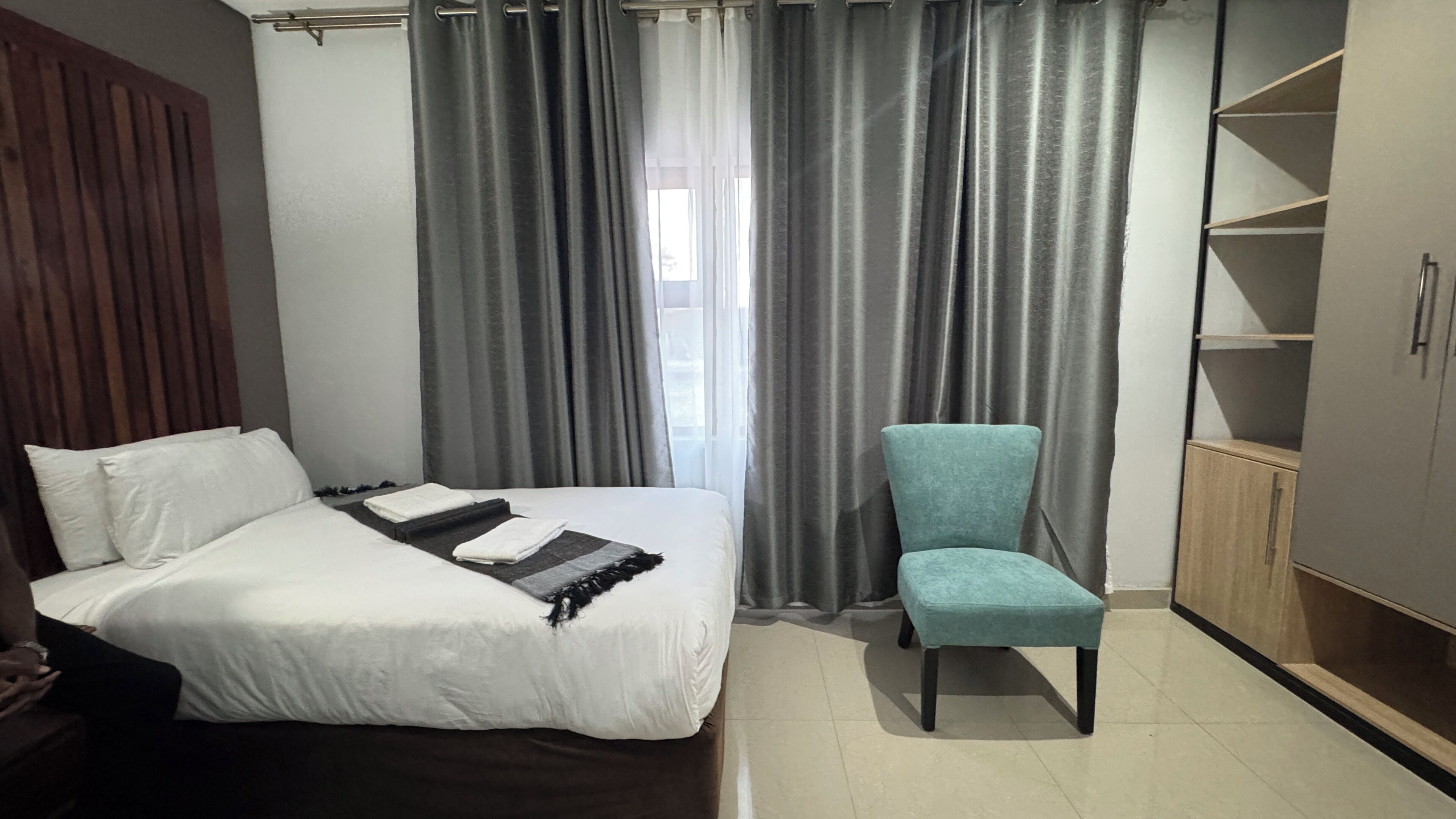 Um quarto com uma cama, uma cadeira, um guarda-roupa e uma janela com cortinas.