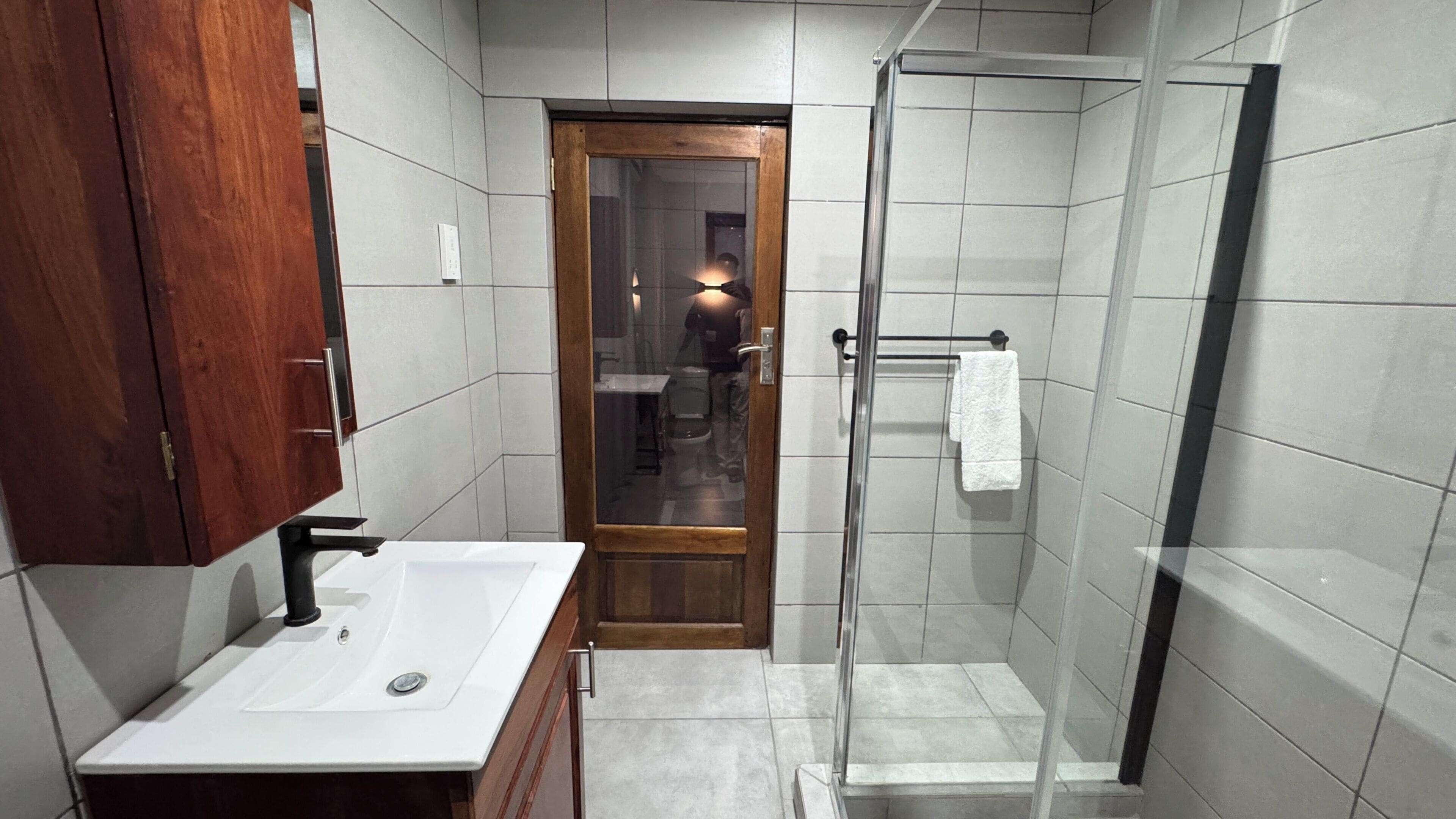 Un baño con un mueble de madera, un lavabo blanco, una cabina de ducha de vidrio y una toalla colgada en un perchero.