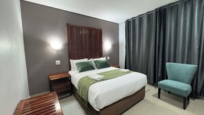 A hotel room with a bed, a chair, a nightstand, and a wall-mounted light. - Raintree Hotel (Nata)