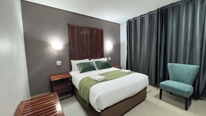 Una habitación de hotel con cama, una silla, una mesita de noche y una lámpara fijada a la pared.