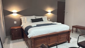 A neatly made bed with a wooden headboard, two bedside tables, a bench, and a chair.