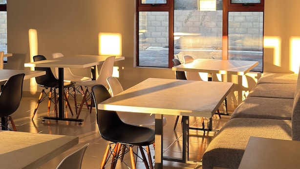 A modern dining area with tables and chairs, large windows, and an air conditioning unit. - Raintree Hotel (Nata)