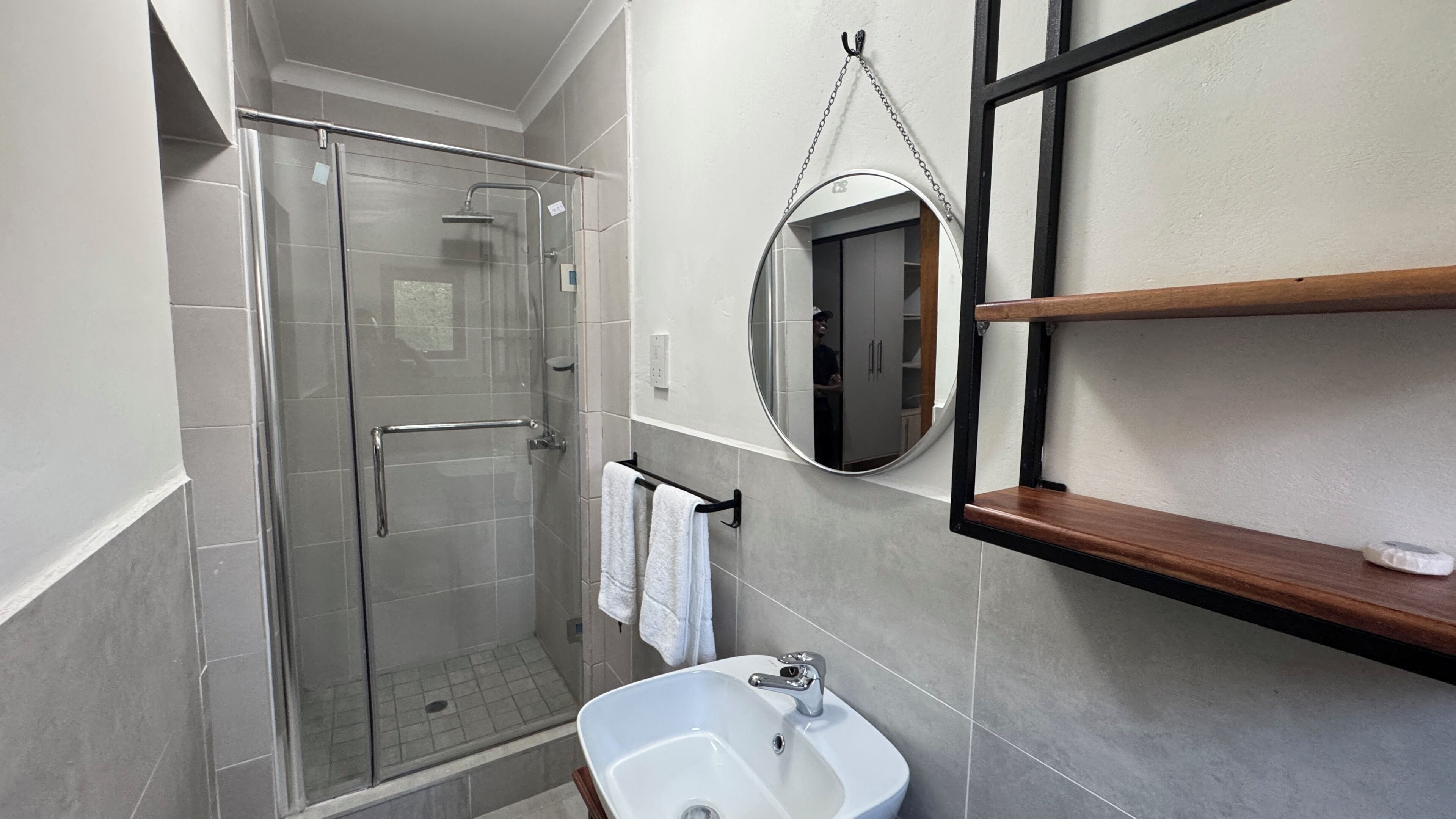 A modern bathroom with a glass shower enclosure, a white sink, and a mirror.
