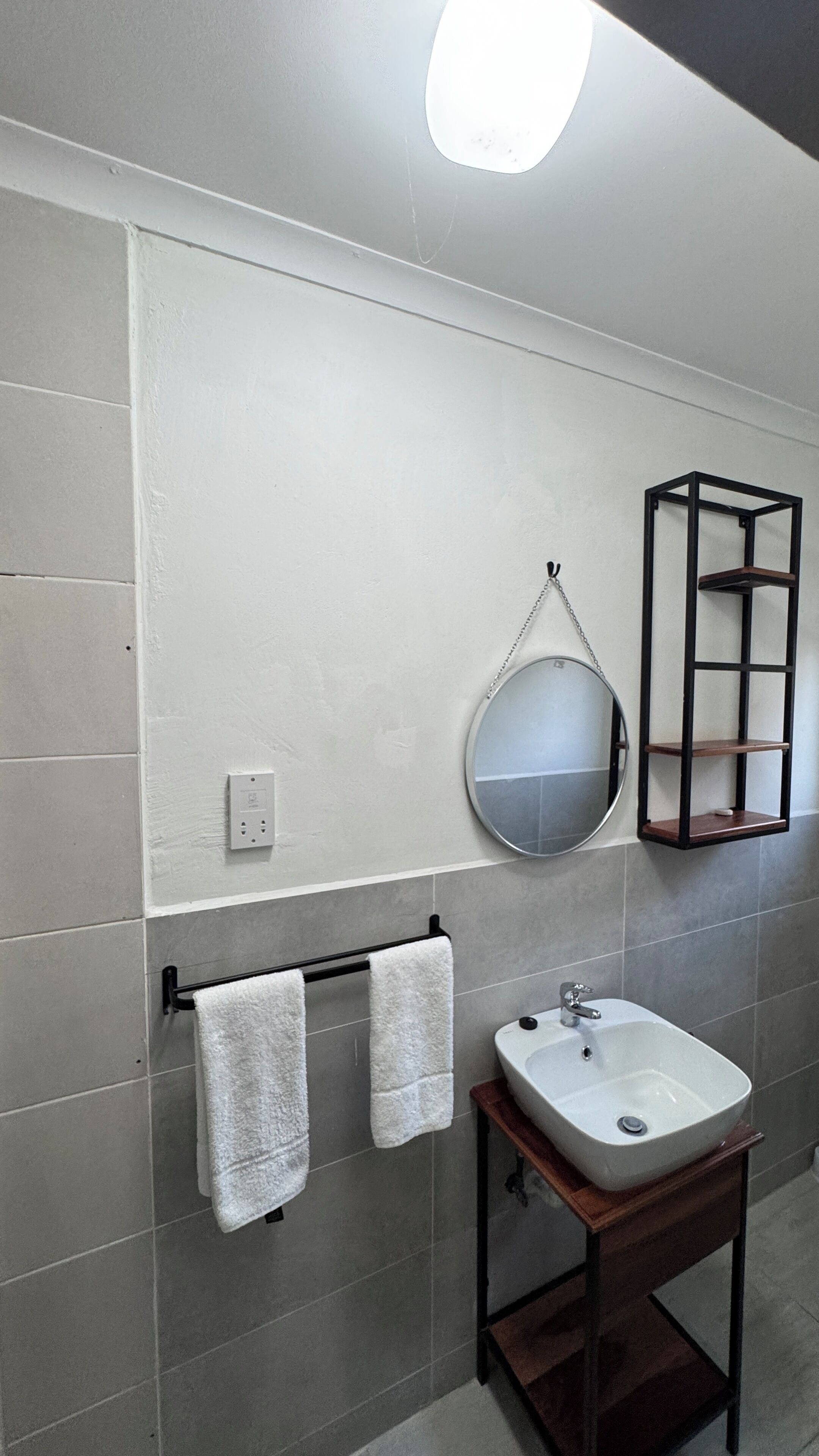 A bathroom with a white sink, a round mirror, and a black shelf.