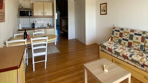 Ein Wohnzimmer mit Sofa, einem Esstisch mit Stühlen, einer Küchenzeile mit Schränken und einer Mikrowelle.
