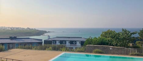 Ein Schwimmbad mit Blick auf das Meer, umgeben von Gebäuden mit einer Metallbedachung.