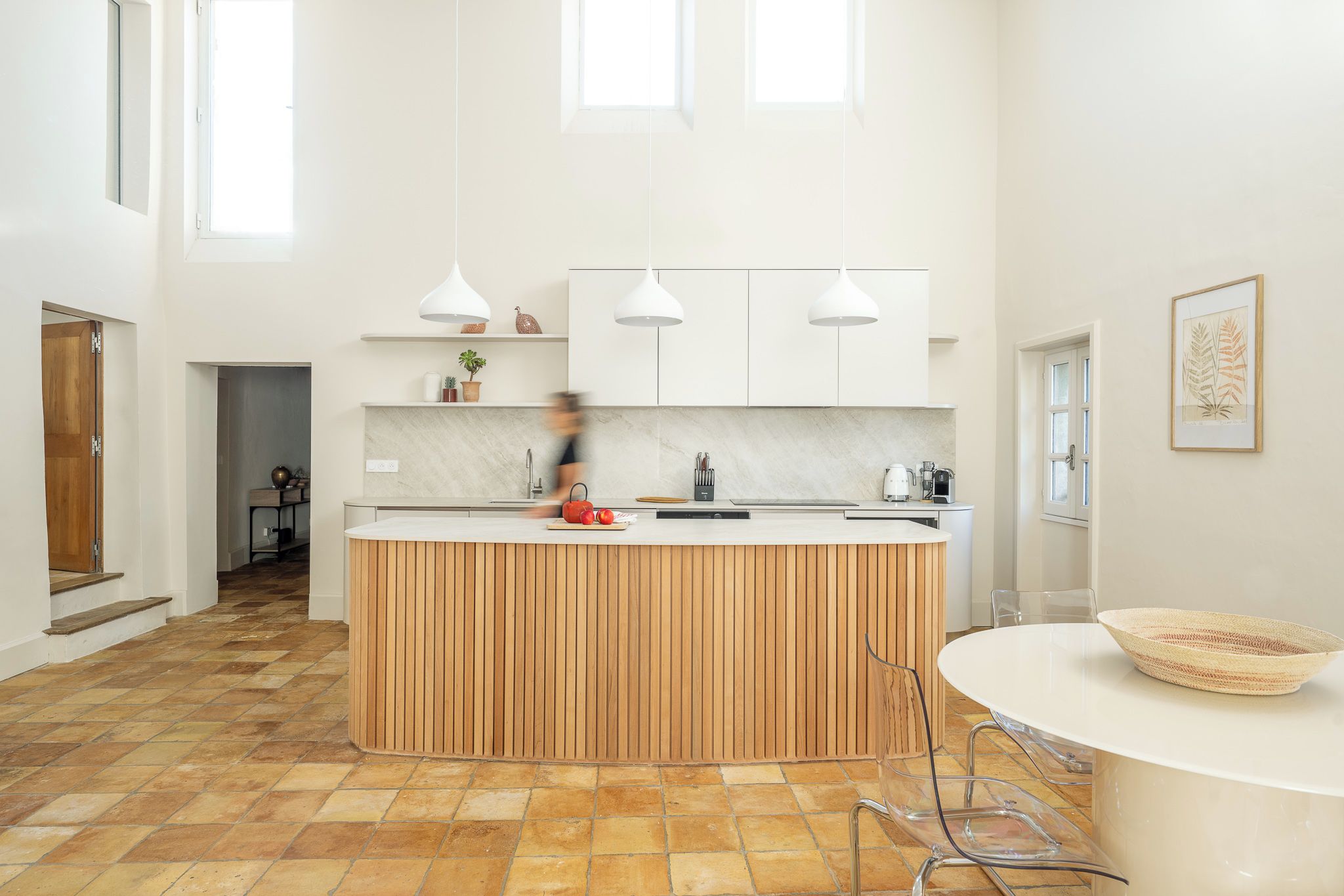 A modern kitchen with a central island, white cabinets, and pendant lighting.