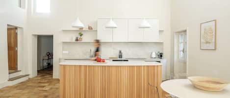 A modern kitchen with a central island, white cabinets, and pendant lighting.