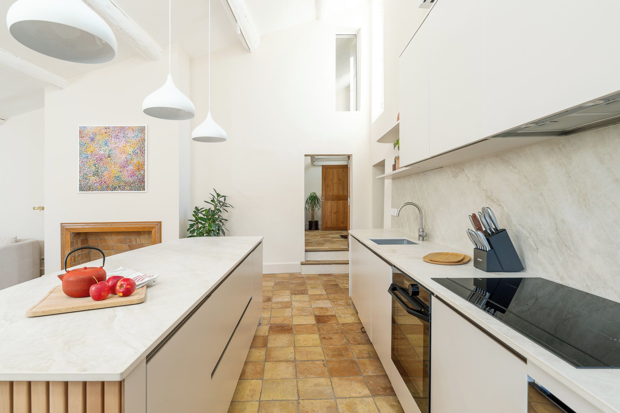 Une cuisine moderne avec des meubles blancs, un îlot central, un four encastré et une grande fenêtre.