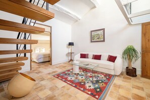 A modern living room with a sofa, a glass coffee table, a patterned rug, and a staircase with wooden railings. - Uzes, Place aux Herbes, Penthouse Le Belvedere , 360 city view Rooftop et clim (Uzès)