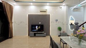A modern living room with a flat-screen TV, a dining area with a marble table, and a staircase with a decorative vase. - Aroma-Pool-Breakfast-Man Thai beach (Da Nang)