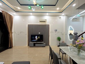 A modern living room with a flat-screen TV, a dining area with a marble table, and a staircase with a decorative vase. - Aroma-Pool-Breakfast-Man Thai beach (Da Nang)