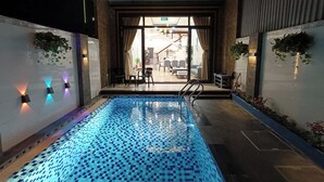 An indoor swimming pool with a tiled floor, a staircase leading to a seating area, and walls with hanging plants. - Aroma-Pool-Breakfast-Man Thai beach (Da Nang)
