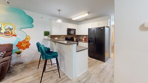 Una cocina con armarios blancos, un refrigerador negro, un microondas y un taburete de bar.