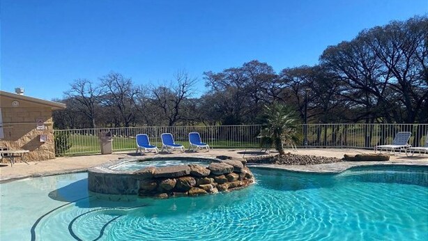Piscina con sillas de descanso, jacuzzi y una fuente de piedra.