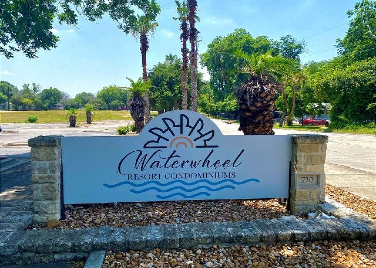 A sign for Waterwheel Resort Condominiums with a logo, name, and address.