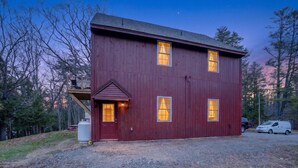 A red building with a porch, a garage, and a gravel driveway. - Forest Backdrop Midcoast Maine Quiet Escape 3 Bedroom Home (Dresden)