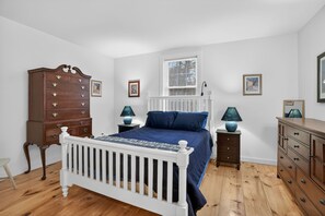 Ein Schlafzimmer mit einem weißen Babybett, einer hölzernen Kommode, einem Nachttisch mit Lampen und einem Fenster mit Jalousien.
