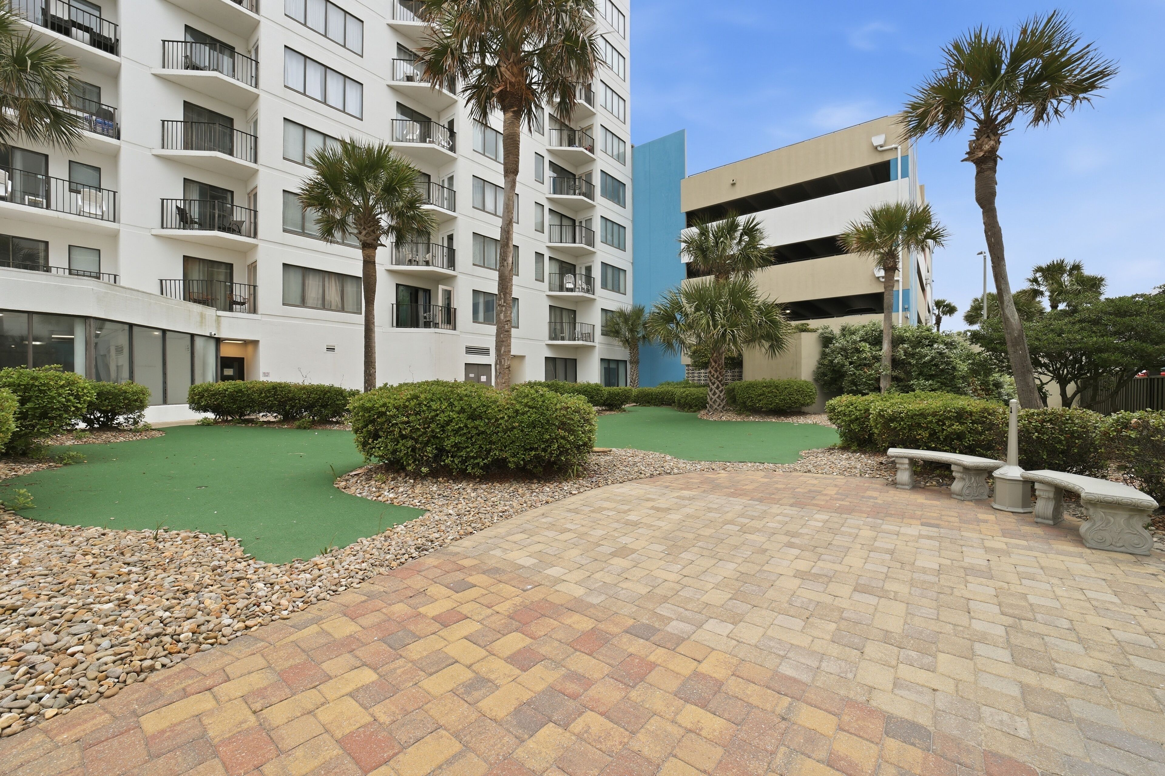 A courtyard with a paved walkway, palm trees, and a building with balconies.