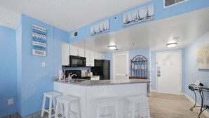 A kitchen with a central island, white bar stools, a microwave, and a refrigerator. - A Coastal Paradise - Beachfront - Gym - Pool (Myrtle Beach)