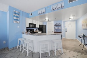 A kitchen with a central island, white bar stools, a microwave, and a refrigerator.