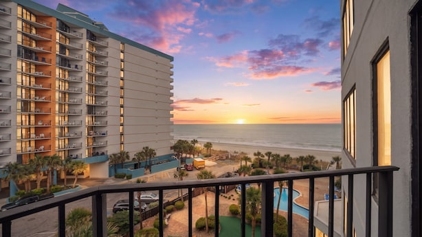 A hotel with a balcony overlooking a pool, a beach, and sunset. - A Coastal Paradise - Beachfront - Gym - Pool (Myrtle Beach)