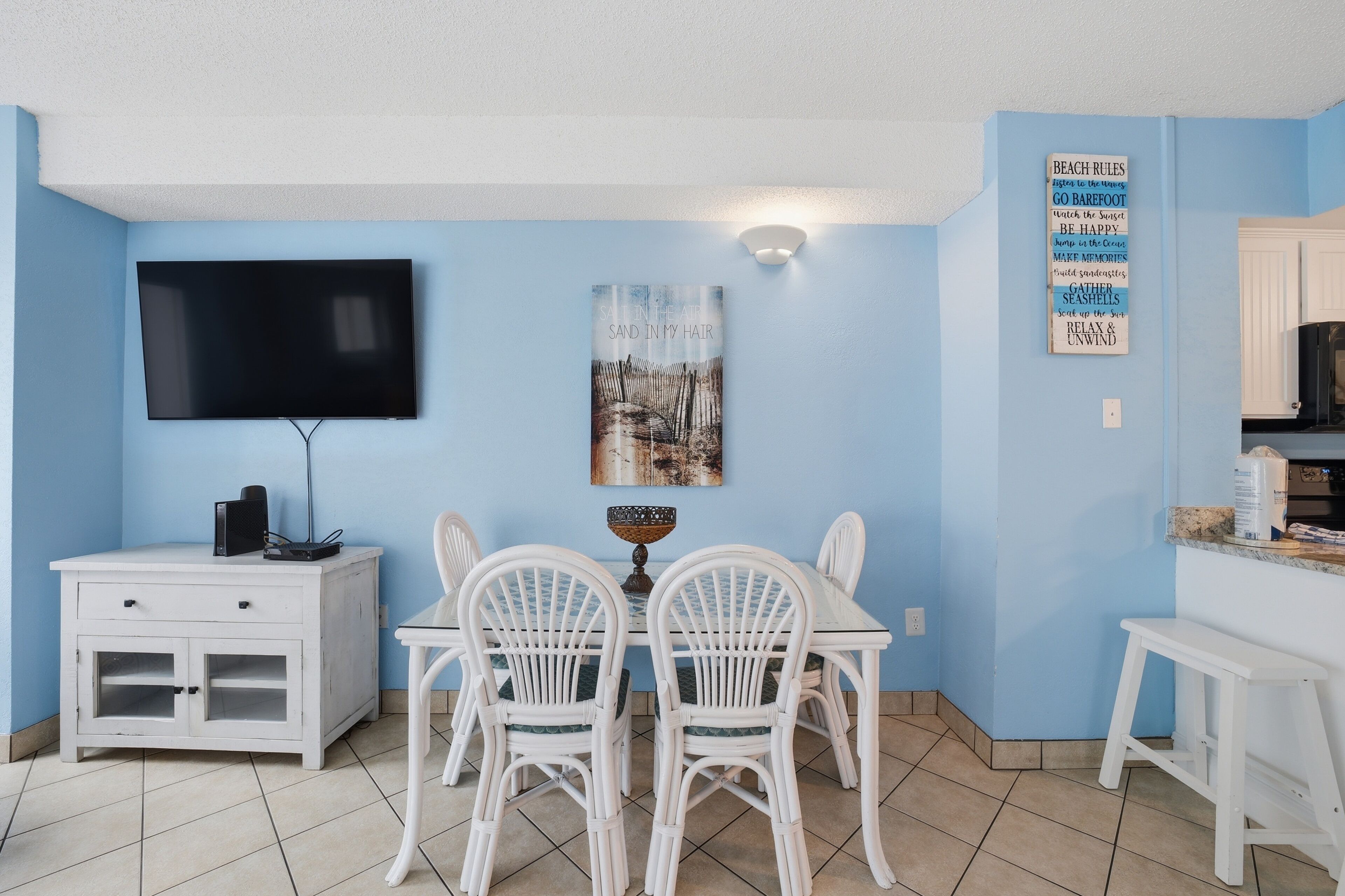 A room with a TV, a dining table with chairs, a cabinet, and a wall with a poster.