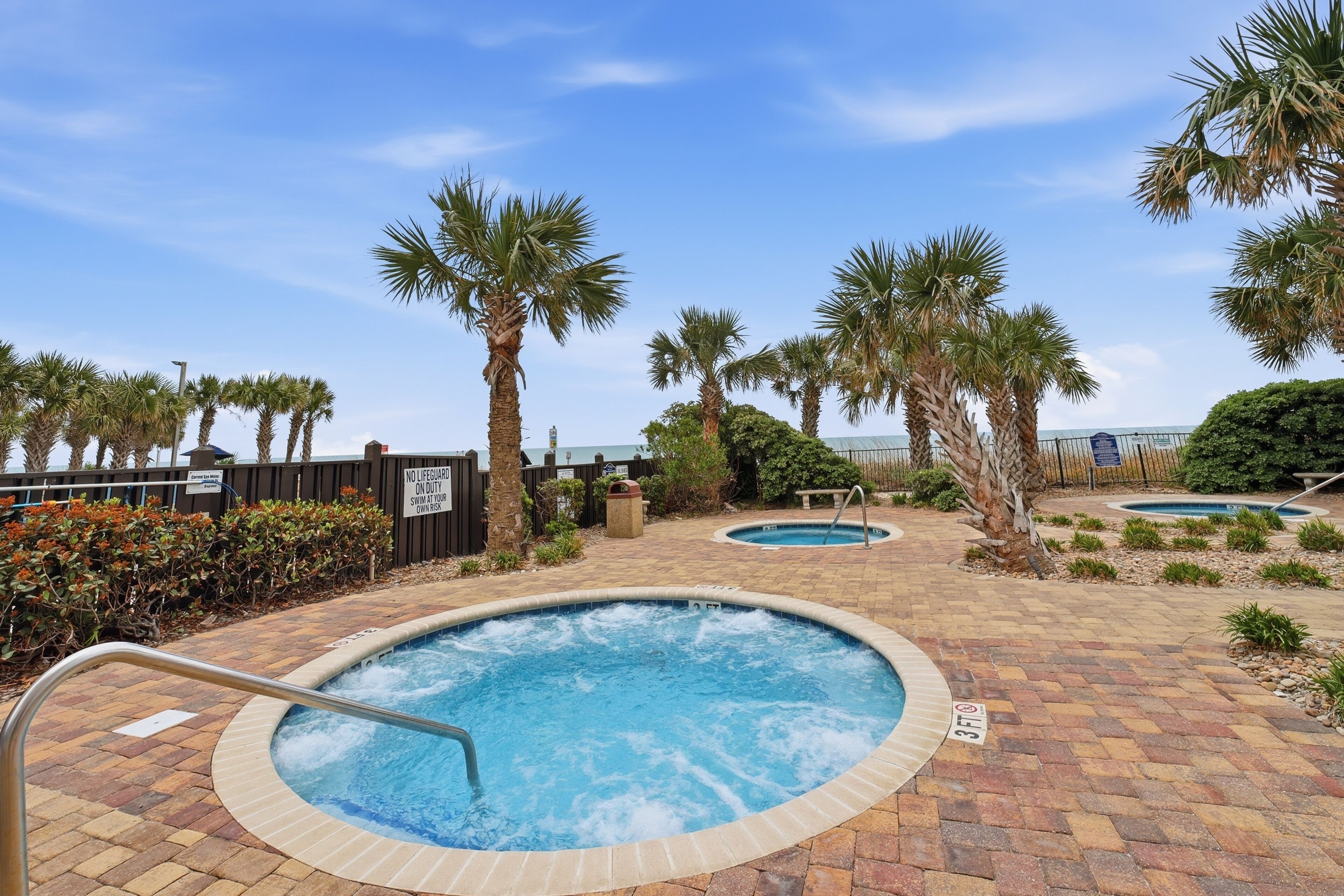 A pool area with two hot tubs, palm trees, and a brick pathway.