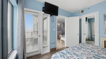 A bedroom with a bed, a television mounted on the wall, and a door leading to another room.