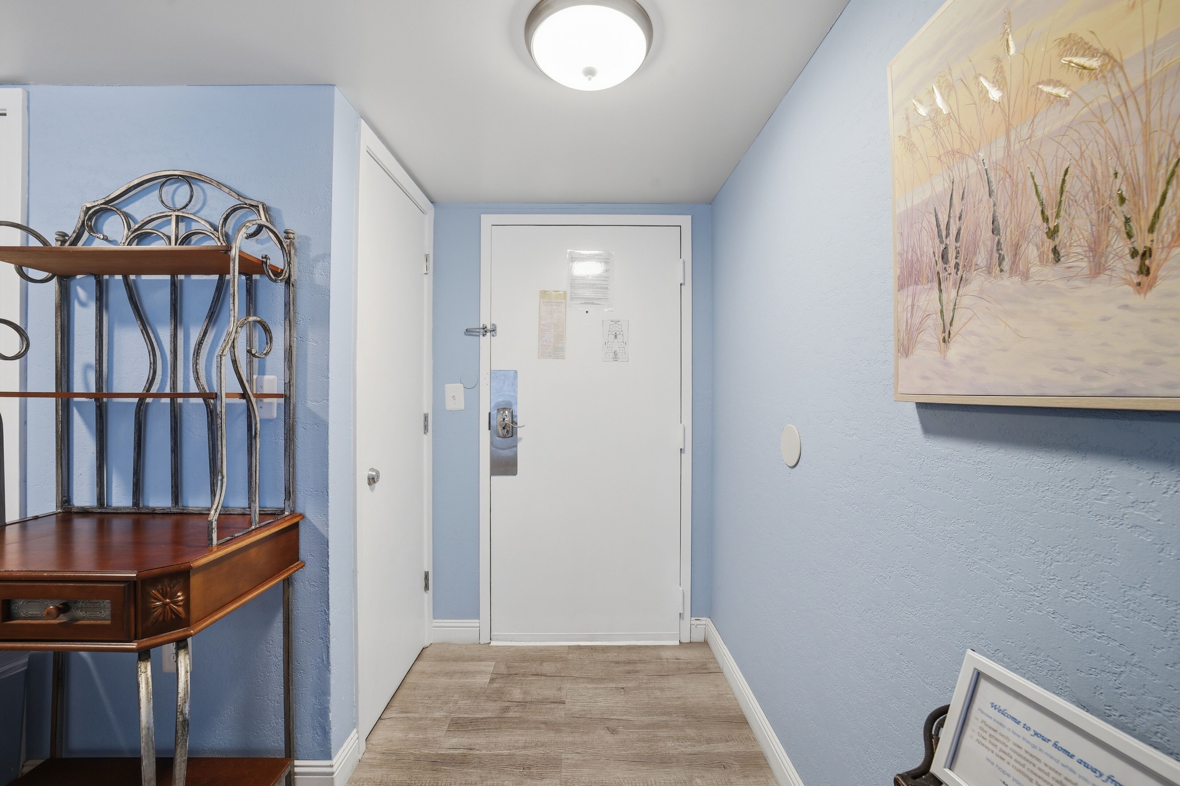 A hallway with a wooden bench, a white door, and a painting on the wall.