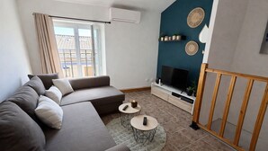 Uma sala de estar moderna com sofá seccional, TV de tela plana, uma mesinha redonda e varanda com vista.