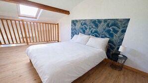 Quarto com piso de madeira, cama com roupa de cama branca, mesa de cabeceira com abajur e cabeceira azul estampada.