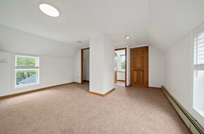 Una habitación amplia con techo alto, un ventanal grande y una puerta que conduce a otra estancia.