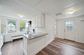 Cucina con mobili bianchi, un piano di lavoro in granito e una finestra con vista su una casa.