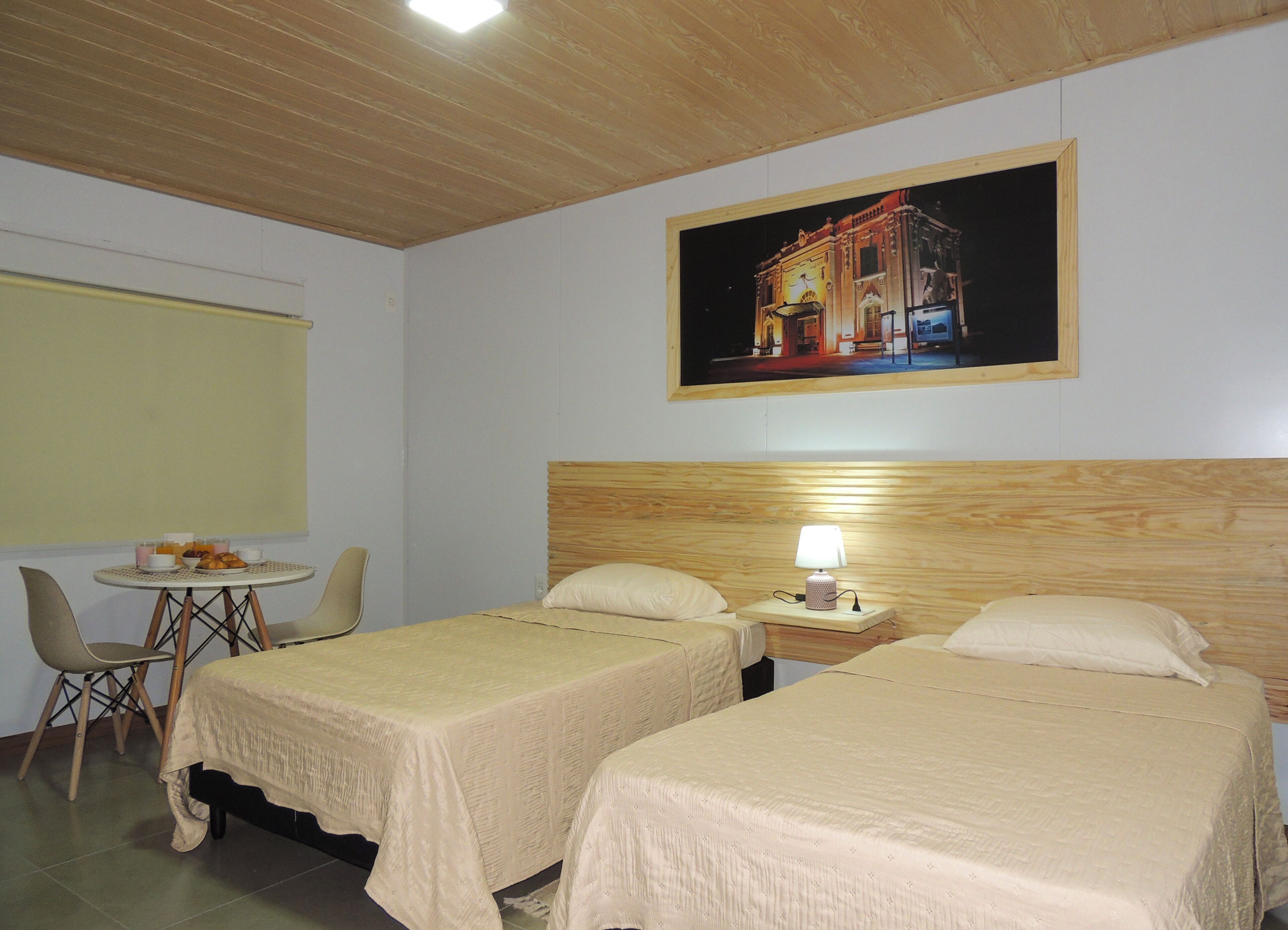 Ein Hotelzimmer mit zwei Betten, einem kleinen Tisch mit Frühstück, einem Stuhl und einem Bild an der Wand.
