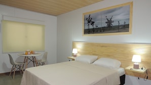 A bedroom with a bed, bedside tables, a chair, a table with drinks, and a painting on the wall. - Jardines Inn (Trinidad)