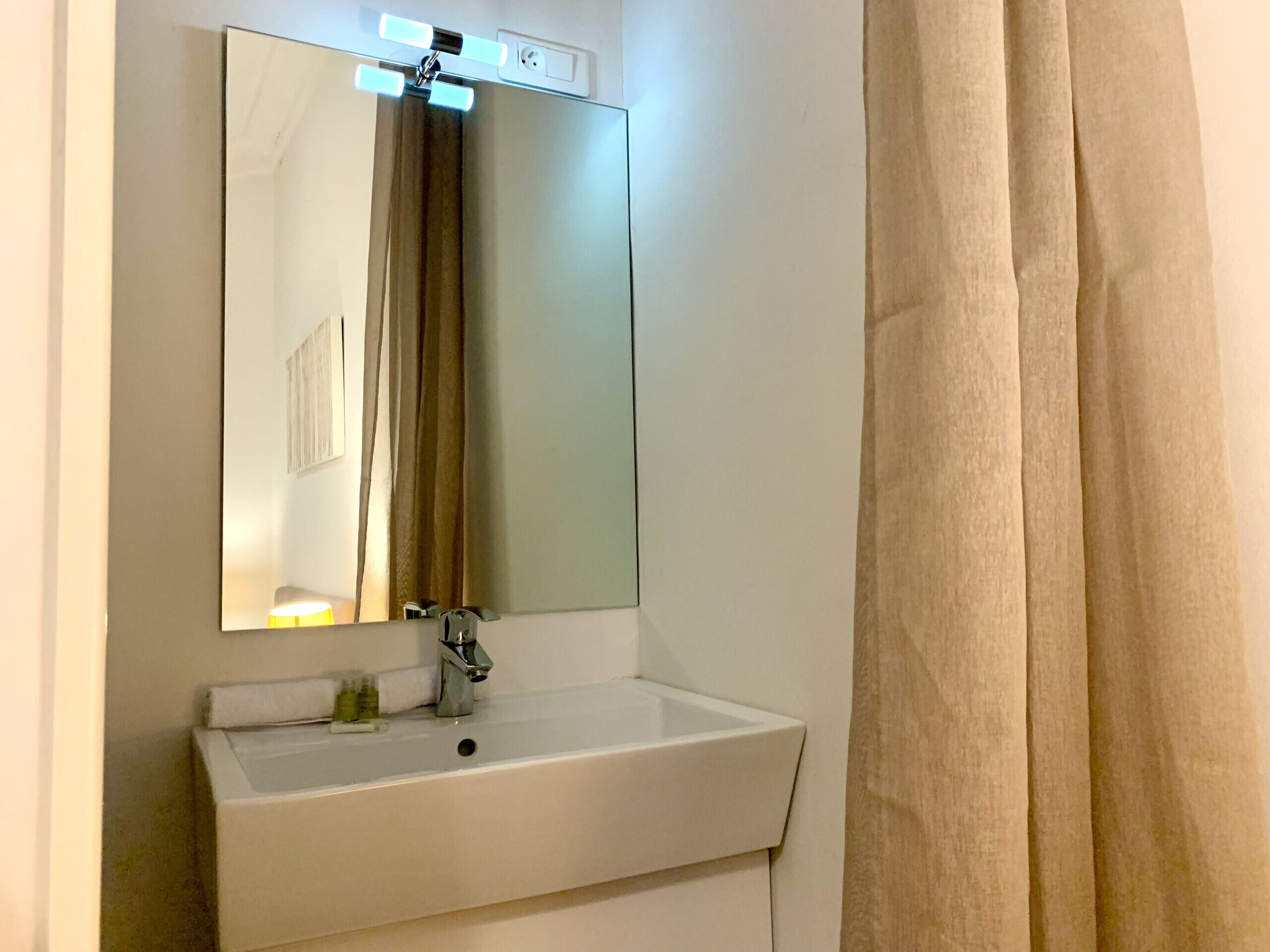 A bathroom with a white sink, a mirror, and a light fixture above the mirror.