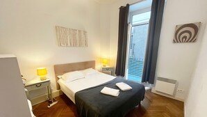 Ein Hotelzimmer mit Bett, Nachttischlampen, einem Fenster mit Vorhängen, einer Heizung und einem kleinen Kunstwerk an der Wand.