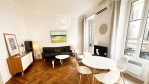 Ein modernes Wohnzimmer mit einer Couch, einem Esstisch mit Stühlen, einer Chandelierleuchtre und einem großen Fenster mit Ausblick.