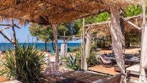 Eine Holzterrasse mit Sitzgelegenheit, einem Reetdach und Blick auf das Meer.