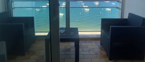 Un balcon doté de meubles en osier, d’une porte vitrée et offrant une vue sur les bateaux qui naviguent.