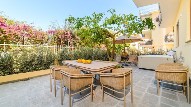 Een terras buiten met een tafel en stoelen, omgeven door planten en een hek.