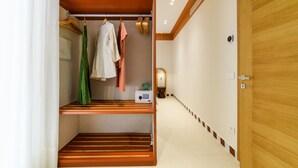 Een inloopkast met houten planken, hangende kleding en een klein elektronisch apparaat op de plank.