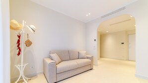 Een moderne woonkamer met een beige bank, een witte vloerlamp en een witte kapstok met hoeden en een klein mandje.