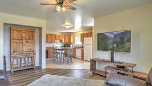 A modern kitchen with wooden cabinets, a dining area with a table and chairs, a living room with a leather sofa, and a large window with a mountain view. - New Listing! Quaint Affordable Cabin | Walkable to Downtown Creede (Creede)