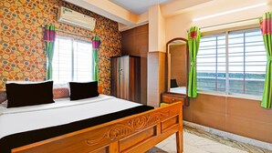 A hotel room with a bed, a wardrobe, a window with curtains, and a wall with a circular pattern. - Deluxe With Ganga View Green Guest House (Shrirampur)