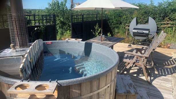 Een hottub op een houten terras met een barbecue en tuinmeubilair.